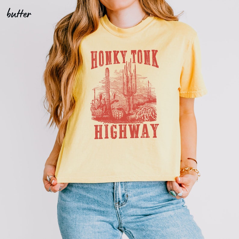May include: Yellow cropped t-shirt with a red graphic print of a desert scene with cacti and the text "Honky Tonk Highway".