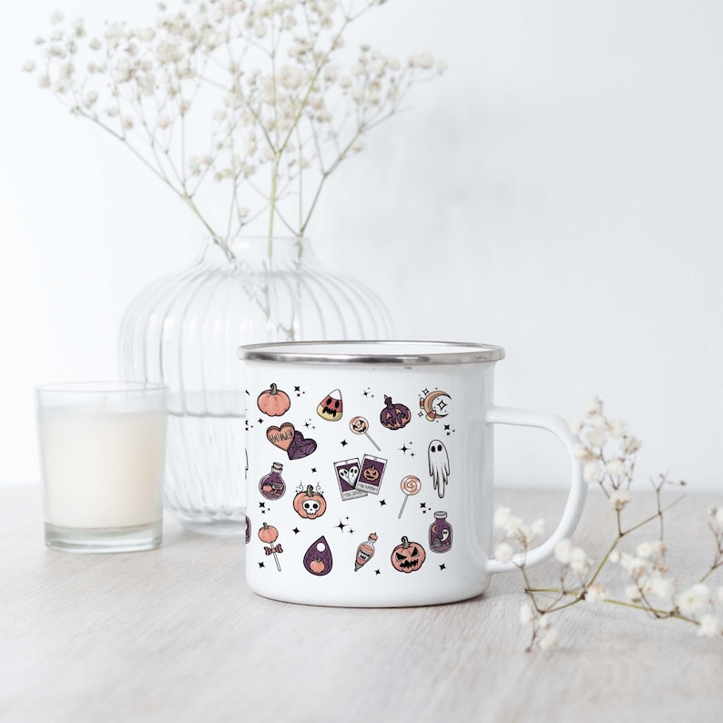 May include: White enamel mug with a Halloween-themed design. The mug features a variety of spooky and cute illustrations, including pumpkins, ghosts, candy corn, and potion bottles. The design is in shades of pink, purple, and black.