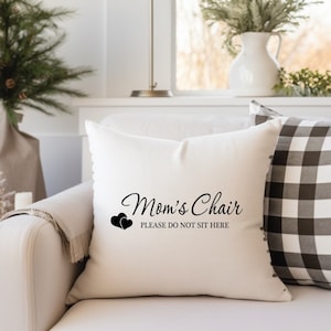 May include: White throw pillow with black text that reads "Mom's Chair Please Do Not Sit Here" with two black hearts above the text.