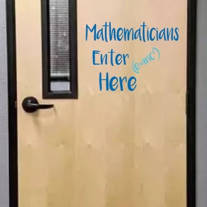 May include: A beige door with a black frame and a silver door handle. The door has a sign that reads "Mathematicians Enter (e=mc²) Here" in blue text.