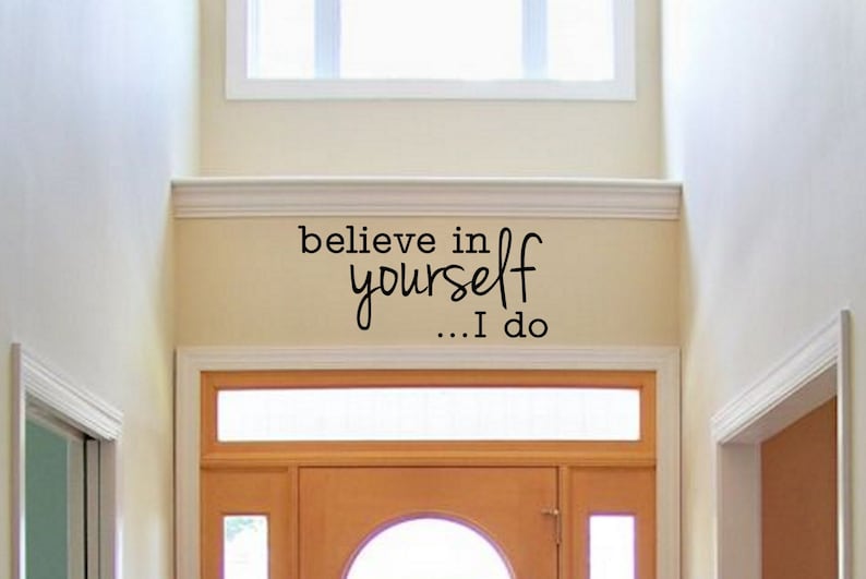 May include: A white wall with a black vinyl decal that reads "believe in yourself... I do". The decal is above a wooden door with a glass window.