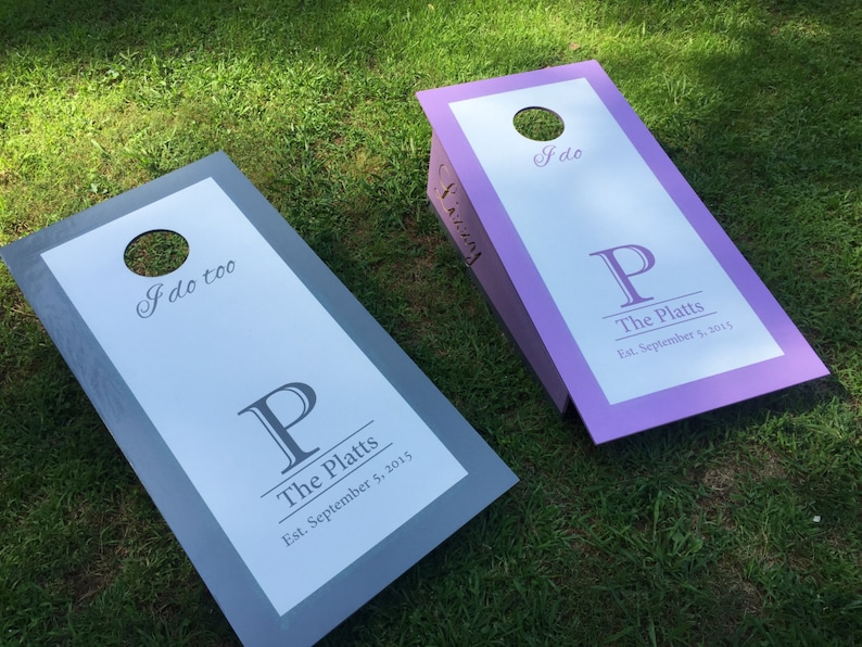 Pode incluir: Duas t&aacute;buas de cornhole de madeira com fundo branco e molduras cinza e roxas. As t&aacute;buas t&ecirc;m o texto "I do" e "I do too" com uma letra "P" grande e o texto "The Platts" e "Est. September 5, 2015".