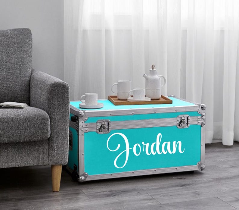 Pu&ograve; includere: Un baule turchese con finiture argentate e il nome "Jordan" in corsivo bianco. Il baule &egrave; usato come tavolino, con un vassoio di legno che contiene tazze bianche e una teiera. Il baule si trova in una stanza con una poltrona grigia.