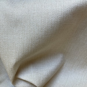 May include: Close-up of a cream-colored fabric with a woven texture. The fabric is smooth and has a subtle sheen.