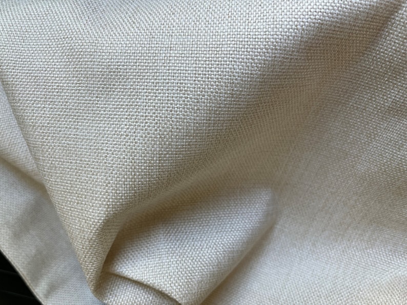 May include: Close-up of a cream-colored fabric with a woven texture. The fabric is smooth and has a subtle sheen.