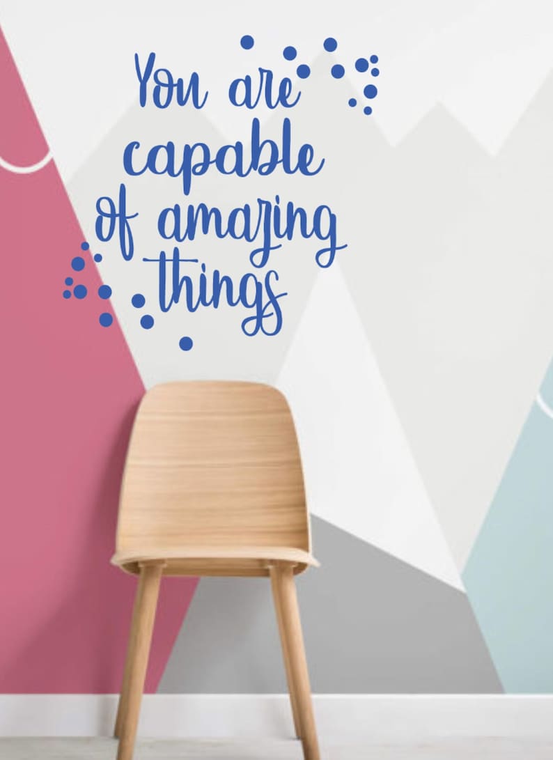 May include: A motivational quote, "You are capable of amazing things", in blue lettering on a white wall with a geometric pattern of pink, gray, and blue. A wooden chair sits in front of the wall.