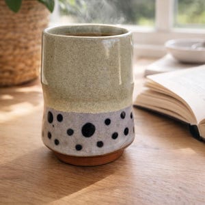 May include: A ceramic mug with a speckled gray and black design, filled with a hot beverage. The mug has a light green upper section and sits on a wooden surface. Steam rises from the mug, suggesting a warm drink.