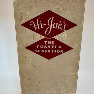 May include: A vintage box for "Hi-Jacs" coasters. The box is a light beige color with a repeating pattern. The front features two red diamond shapes with white text that reads "Hi-Jacs" and "The Coaster Sensation". The bottom of the box reads "The Killinger Company, Marion, Virginia."