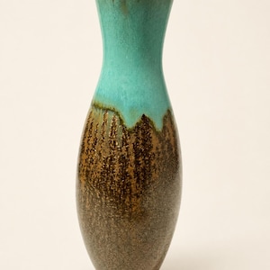 May include: A tall ceramic vase with a narrow neck and a rounded body. The upper portion features a smooth, bright turquoise glaze, while the lower section displays a textured, mottled brown and dark earth-toned finish with a visible crackle pattern.
