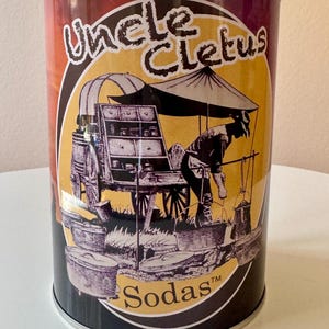 May include: A vintage-style metal tin with a colorful design featuring a cartoon image of a man selling sodas from a cart. The text "Uncle Cletus Sodas™" is printed on the tin.