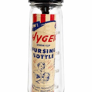 May include: Vintage Hyge screw-top nursing bottle. The clear glass bottle has a black cap and a paper label with red, white, and blue accents. The label reads "NEW! Hyge Screw-Top Nursing Bottle" with an illustration of a woman.