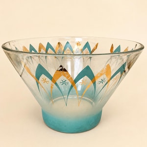 May include: A clear glass bowl with a wide, flared rim and a frosted turquoise base. The exterior features a repeating pattern of pointed teal arches alternating with gold leaf-style shapes, each containing a small, stylized teal starburst icon.