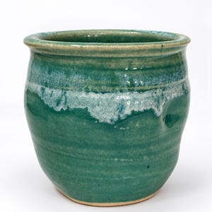 May include: A ceramic pot with a rounded body and a wide opening, featuring a glossy green glaze with a distinct white drip pattern around the upper rim. The base of the pot is unglazed, showing the natural tan color of the clay material.