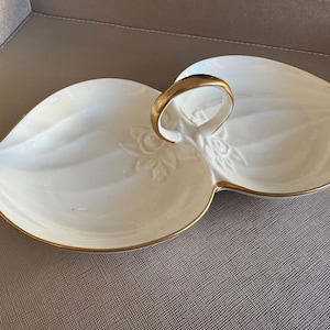 May include: A white ceramic serving dish with a gold rim and a gold handle. The dish is divided into two sections and has a floral design.