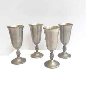 May include: Four vintage pewter goblets with a classic design. Each goblet features a flared rim, a detailed stem, and a round base. The goblets are displayed on a white surface.