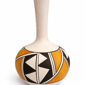 May include: A handcrafted ceramic vase with a cream-colored neck and a rounded body. The body features a geometric design in black, white, and orange. The vase has a narrow neck and a wide base.