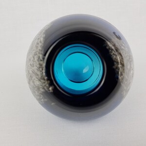 Puede incluir: Un jarr&oacute;n redondo de vidrio negro con un dise&ntilde;o de espiral blanco. El jarr&oacute;n tiene una abertura de vidrio azul.