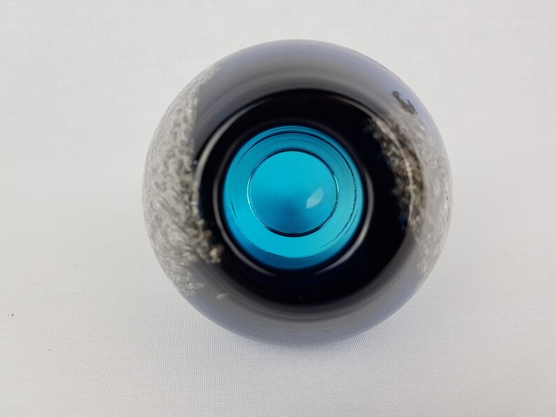 Puede incluir: Un jarr&oacute;n redondo de vidrio negro con un dise&ntilde;o de espiral blanco. El jarr&oacute;n tiene una abertura de vidrio azul.