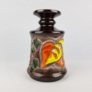 Peut inclure: Un vase en céramique brun avec une base large et un col étroit. Le vase est décoré d'un motif floral coloré dans les tons orange, jaune et vert.