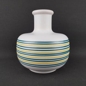 May include: A white ceramic vase with a rounded body and a narrow neck. The vase is decorated with horizontal stripes of teal and yellow. The vase is approximately 8 inches tall.