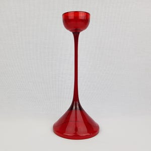 Peut inclure: Un bougeoir en verre rouge, haut et évasé, avec une base évasée et un sommet cylindrique étroit.