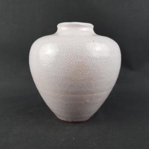 Könnte beinhalten: Eine weiße Keramikvase mit Craquelé-Glasur. Die Vase hat einen abgerundeten Körper und einen schmalen Hals. Der Boden ist rotbraun. Die Vase ist ein dekorativer Gegenstand.