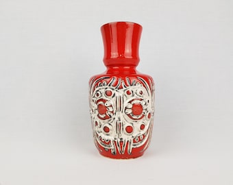Puede incluir: Un jarrón de cerámica rojo con un diseño geométrico blanco y negro. El jarrón tiene una base ancha y un cuello estrecho.