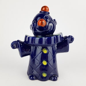 May include: A blue ceramic clown figurine with a red nose and yellow buttons. The clown is wearing a blue and yellow costume and has a red hat.
