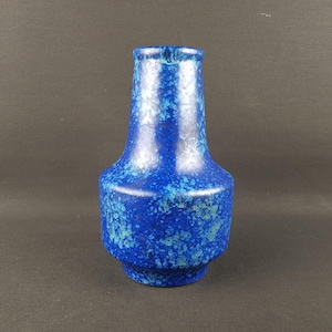 May include: A ceramic vase with a wide, rounded base that tapers upwards to a narrow neck. The surface features a mottled glaze in shades of deep cobalt blue, royal blue, and lighter turquoise, creating a textured, speckled appearance throughout.