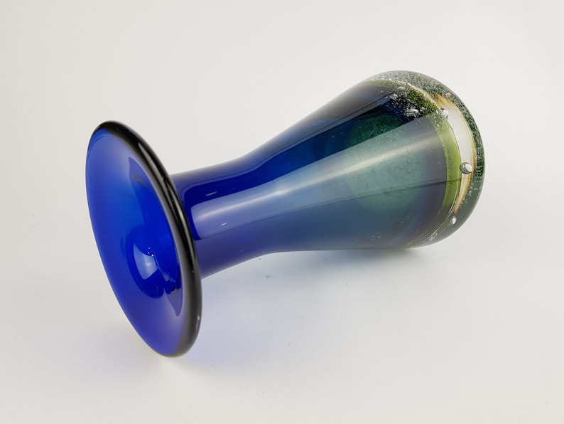 May include: A blue glass vase with a flared base and a green and white swirl design.