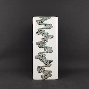 May include: A rectangular white ceramic vase with a vertical design of interconnected, cloud-like shapes in black and teal. The vase has a glossy finish and stands against a dark background.
