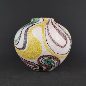 May include: A white ceramic vase with a rounded shape and a swirling abstract design in yellow, green, black, and brown.
