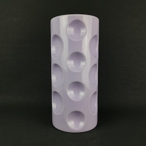 May include: A cylindrical, lavender-colored vase with a repeating pattern of raised, circular indentations. The vase is smooth and glossy, with a simple, modern design. The vase is suitable for displaying flowers or as a decorative accent.