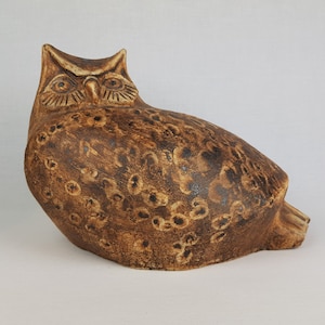 Könnte beinhalten: Eine Keramik-Eulen-Skulptur mit brauner und schwarzer gesprenkelter Glasur. Die Eule hat große, runde Augen und einen detaillierten Schnabel.