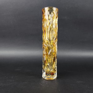 Peut inclure: Un vase en verre cylindrique et long, avec un motif texturé semblable à de l'écorce. Le vase est principalement de couleur ambre, avec des stries de verre blanc et transparent. Le design rappelle l'écorce d'arbre. Le vase est adapté pour exposer des fleurs.