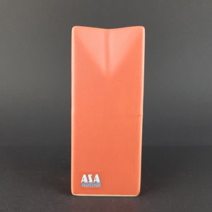 Può includere: Un vaso in ceramica alto e rettangolare di colore arancione terracotta uniforme. Il bordo superiore presenta una distinta rientranza a forma di V. Una piccola etichetta rettangolare nell'angolo in basso a sinistra mostra il testo bianco ASA SELECTION.