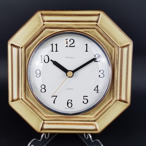 May include: A gold octagonal clock with a white face and black hands. The clock face has black numbers and the words "Kienzle" and "Quartz" printed on it.