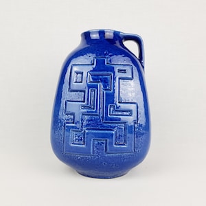 May include: A cobalt blue ceramic vase with a geometric design and a handle. The vase has a textured surface.