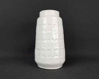 May include: White ceramic vase with a geometric pattern. The vase has a cylindrical shape and a wide mouth.