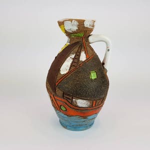 May include: A brown ceramic pitcher with a white handle and a painted design of a ship with orange, blue, and green accents.