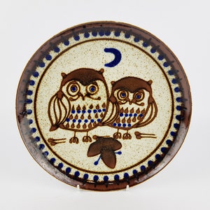 May include: A ceramic plate with a brown and blue border and a design of two owls with blue eyes and a crescent moon. The owls are brown with white accents and blue and brown spots.
