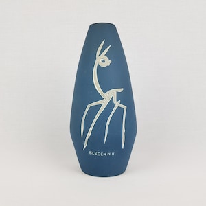 May include: A blue ceramic vase with a white stylized deer design. The vase is signed "BERGEN N.H."