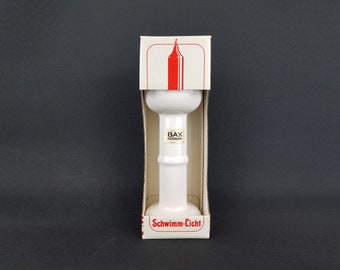 May include: White ceramic candle holder with a red candle inside the box. The box has the text "BAY. KERAMIK" and "Schwimm-Licht" printed on it.