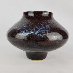 Peut inclure: Un vase en céramique brun foncé avec un glaçage moucheté et des accents bleus et blancs. Le vase a une base large et ronde et un col étroit.