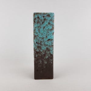 Peut inclure: Un vase en céramique rectangulaire et haut avec une surface texturée et poreuse. La partie supérieure présente un émail turquoise vif qui se transforme en une base brun mat foncé, créant un dégradé de couleurs bicolore sur la forme verticale.