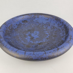 Op de afbeelding: Een grote, ronde keramische kom met een diepblauwe glazuur en een gekrakelde afwerking. De kom heeft een donkerblauwe rand en een gevlekte uitstraling.
