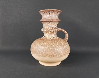 May include: A brown and beige ceramic vase with a textured surface and a handle. The vase has a wide base and a narrow neck.