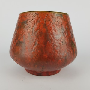 Puede incluir: Un jarrón de cerámica rojo con una superficie texturizada. El jarrón tiene una base ancha y una abertura estrecha.