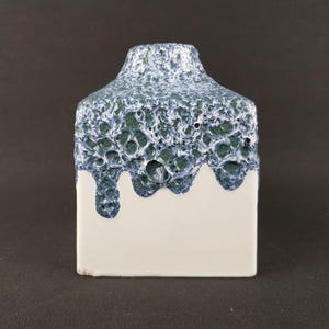 May include: A square ceramic vase with a textured, dark teal and white glaze. The top portion has a bubbly, porous texture, while the bottom half is smooth white. The vase has a narrow neck and a modern, minimalist design.