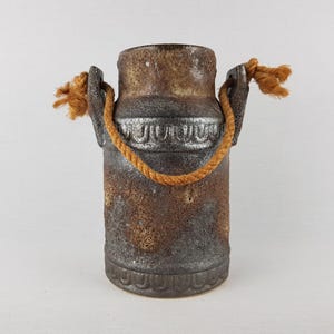 Może przedstawiać: Ruska ceramiczna mleczarka w kolorze brązowym i szarym z uchwytem z sznurka. Mleczarka ma ozdobny srebrny pasek wokół środka.